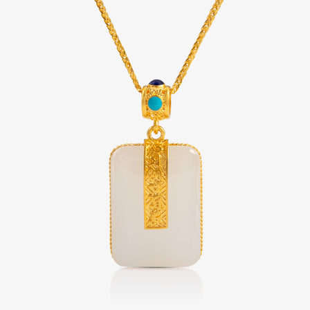 A 24K Gold and Nephrite Pendant with a rectangular nephrite stone adorned by 24K gold detailing and an engraved six-syllable pattern. The bail is accented with turquoise and sapphire stones for added elegance.