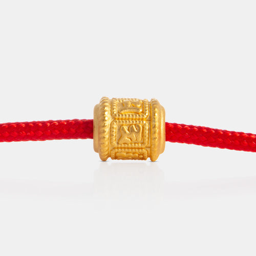 24K Gold Six-Syllable Cylinder Charm on a red knot bracelet